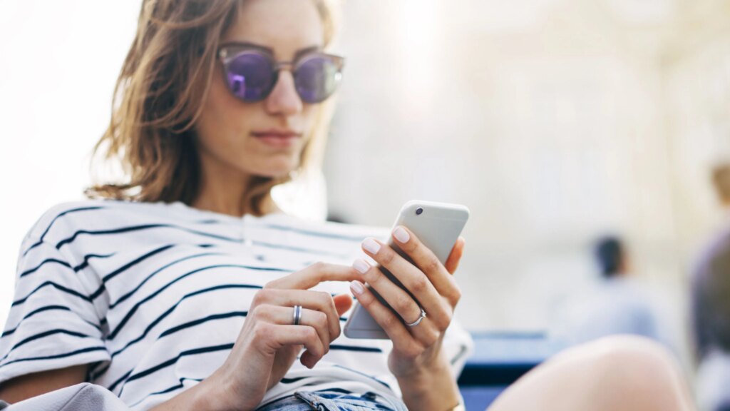 Frau mit Sonnenbrille schaut auf ihr Smartphone