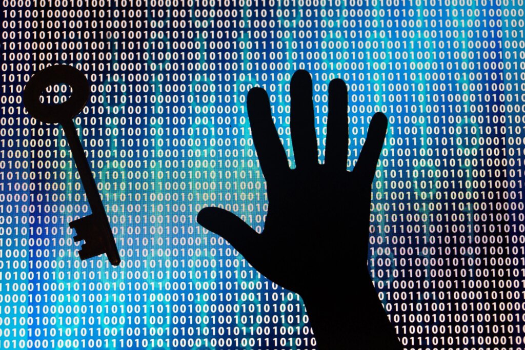 Tech Companies Call for Improved Cyber Defenses After AI-Enabled Attacks Silhouette of a hand with splayed fingers next to a silhouette of a key. In the background, code scrolls by.