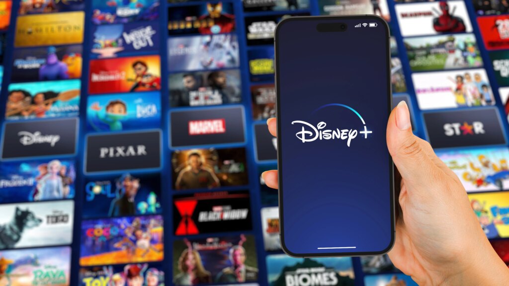 The Disney Plus App Is Getting TikToks. Is a Free Plan Next? Disney Plus logo on smartphone in front of background that shows Disney franchises