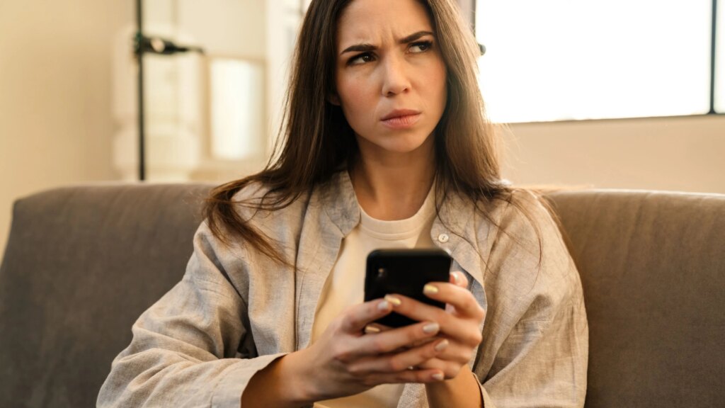 Unlimited-Tarif für 14,99 € im Monat – zu gut, um wahr zu sein? Frau sitzt auf der Couch mit ihrem Handy in der Hand und blickt kritisch