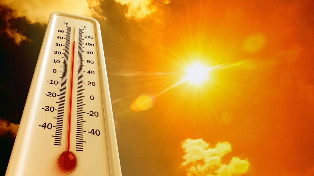 Was tun bei Hitze? 5 Dinge, die helfen können Thermometer auf der hohe Temperatur angezeigt wird, im Hintergrund eine grelle Sonne