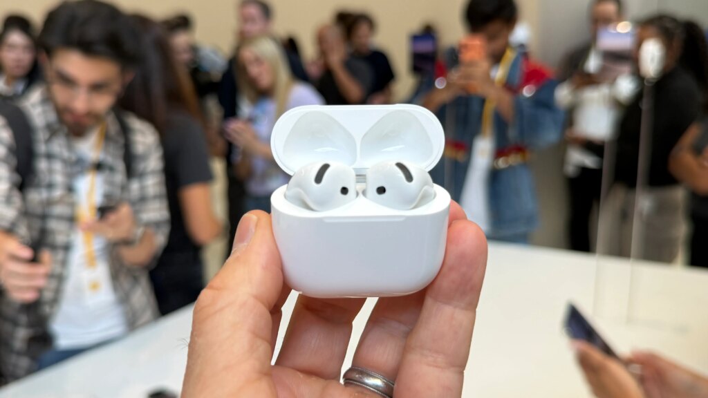 The AirPods 5 shown in their case with the case open the CNET reviewer's hand.