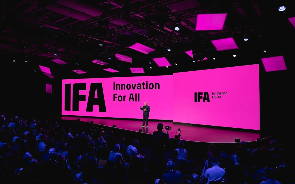 Das sind unsere Editors’ Choice Gewinner der IFA 2026 Ein Redner steht auf einer großen Bühne vor zwei pinkfarbenen Leinwänden mit der Aufschrift „IFA Innovation For All