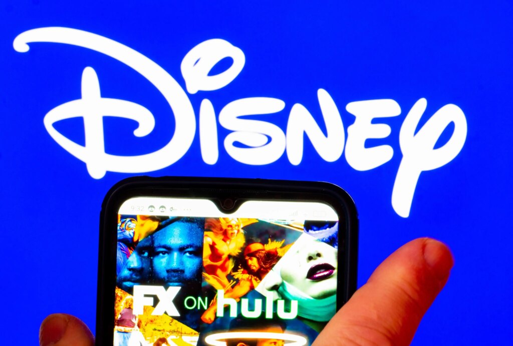 Disney Plus and Hulu Prices Go Up, With Ad-Free Plans Hit the Hardest hulu on phone in front of Disney logo