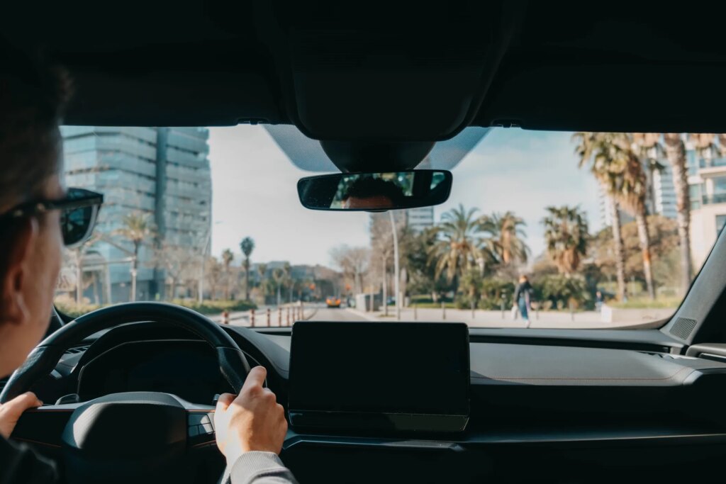 Ride-sharing driver navigating through a modern city with palm-tree-lined streets and urban buildings visible through the windshield.