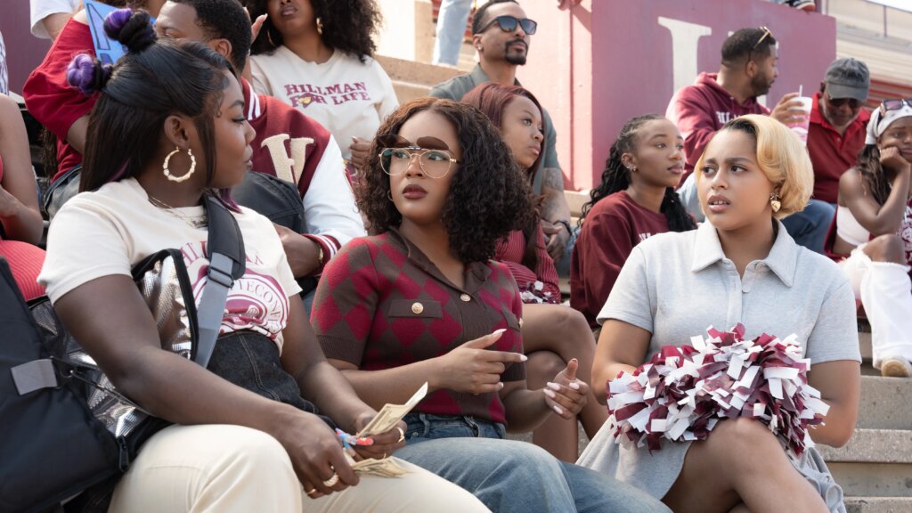 Netflix’s ‘A Different World’: Season 1 Review Alijah Kai as Rashida, Maleah Joi Moon as Deborah, Kennedi Reece as Hazel in A Different World, sitting on bleachers at a game.