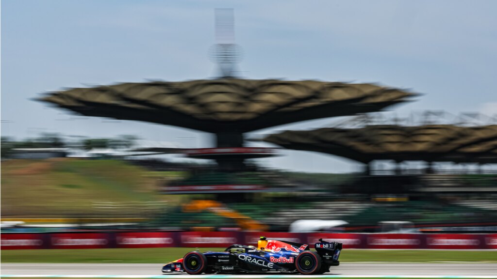Max Verstappen driving an Oracle Red Bull Racing F1 car, with the racing track background blurred in the distance.