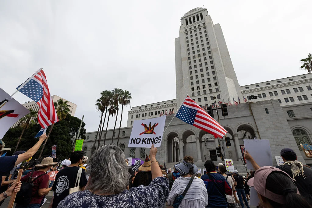 Meta Blames Bot Traffic for No Kings Day Instagram Suspension Protesters at a Los Angeles rally hold up flags and a NO KINGS sign with a crown crossed out in front of a large building.