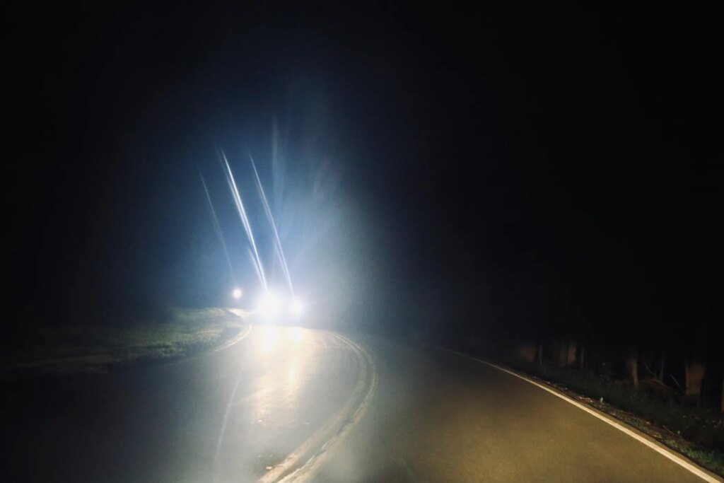 From the perspective of the driver, headlights shine brightly from oncoming traffic at night.