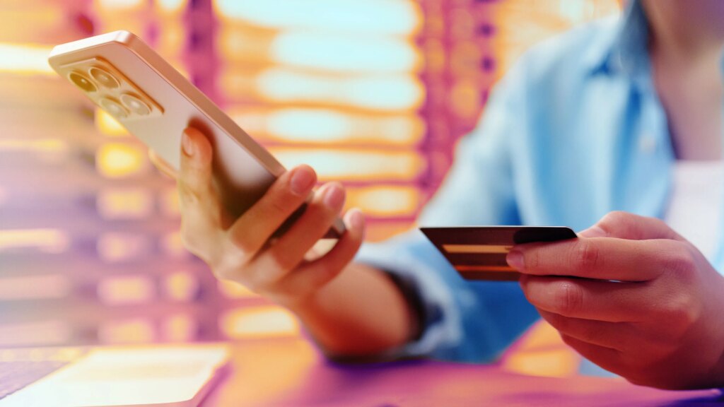 Yes, You’re Probably Paying More for Phone Service. Here’s Where Your Money Is Going Closeup of a person holding a smartphone in one hand and a credit card in the other.